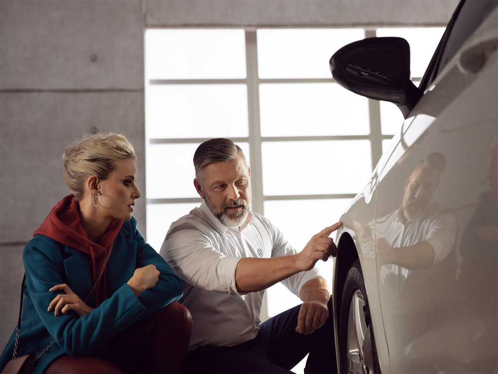 Addetto alle vendite Volkswagen controlla la carrozzeria dell'auto Volkswagen insieme alla cliente